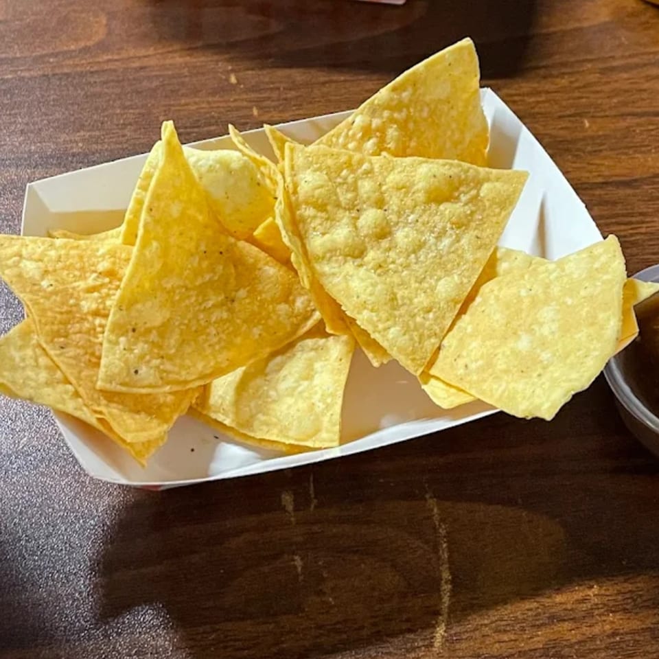 A white paper tray filled with golden tortilla chips, next to a small cup of salsa.