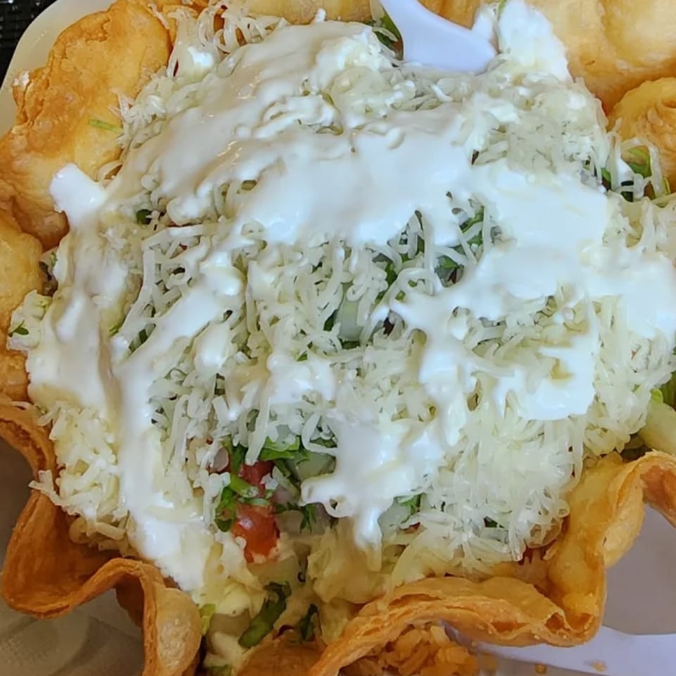A Mexican taco salad in a crispy fried tortilla bowl, topped with shredded cheese and sour cream.