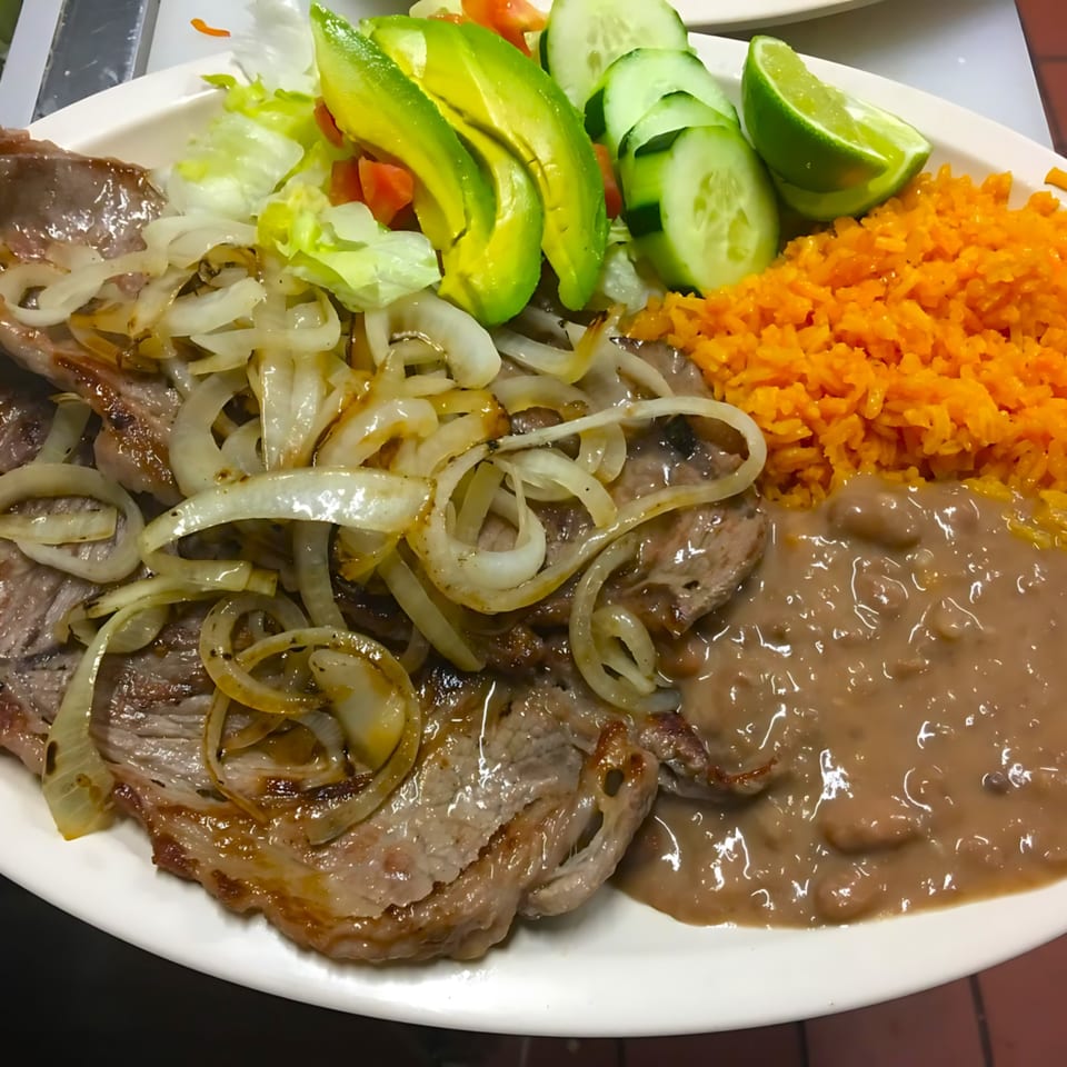 Cocina Doña Chuyita's carne asada with grilled onions, rice, refried beans, and a side salad.