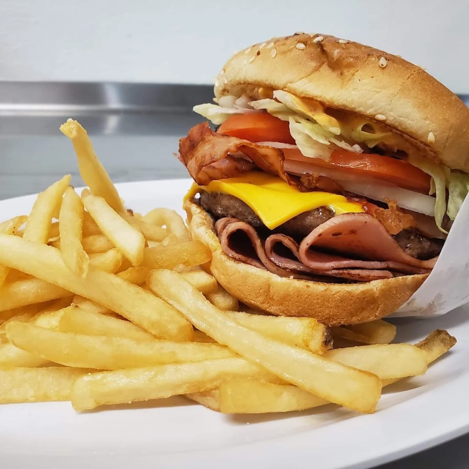 A large burger with cheese, bacon, ham, lettuce, tomato, and onion, served with fries.
